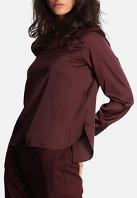 Blusa rossa a maniche lunghe in tessuto morbido con scollo rotondo, spacco laterale e vestibilità comoda, abbinata a pantaloni coordinati.