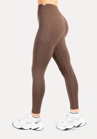 Brune højhøjede leggings i en glat, elastisk stof med en tætsiddende pasform. Kombineret med chunky hvide sneakers.