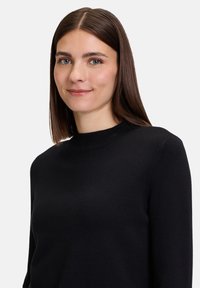 Čierny pletený sveter s okrúhlym výstrihom a dlhými rukávmi, ktorý sa vyznačuje hladkou textúrou a priliehavým strihom. Jednoduchý a klasický dizajn.