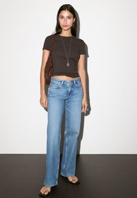 Braunes cropped T-Shirt, hellblaue weit geschnittene Jeans, braune geflochtene Umhängetasche, silberne Anhängerkette und schwarze flache Sandalen.