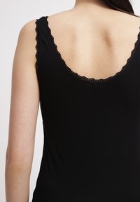 Svart linne med rundad rygg, prytt med en delikat spetskant längs halsringning och ärmhål, tillverkat av ett mjukt, stretchigt material.