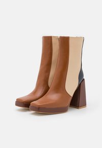 Bottes chevilles en cuir marron et beige avec un talon bloc, présentant une texture lisse, un bout carré et un design à blocs de couleur verticale.