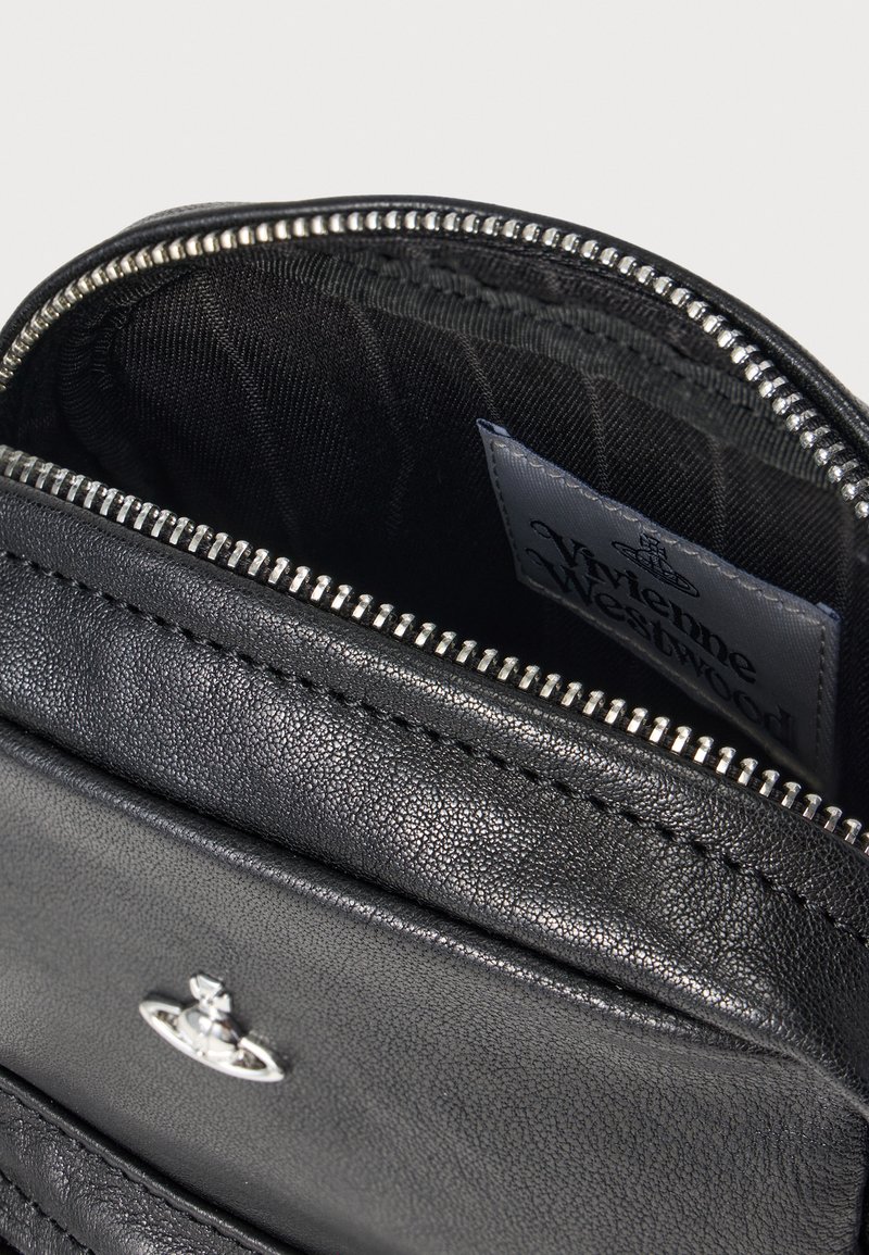 Inderside af sort lædertaske med lynlåslukning, tekstureret stoffor og et mærke med "Vivienne Westwood" trykt på.