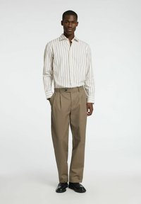 Pasiasta koszula z długim rękawem w jasnych tonacjach, z kołnierzykiem. Spodnie z beżowej tkaniny, z przednim fałdą i zapięciem na guzik. Czarne buty.