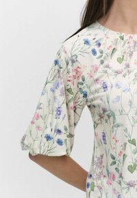 Blomstermønster top med korte puffærmer, der har en lys creme baggrund og en række pink, lilla og grønne botaniske mønstre.