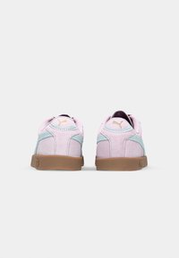 Růžové semišové tenisky s světle modrými akcenty, zaoblený tvar, gumové podrážky a logo na patě. Zadní pohled ukazuje polstrovaný límec a šev.