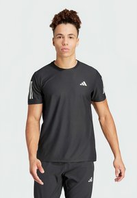 Camiseta atlética preta de mangas curtas, feita de material respirável. Apresenta o logo branco da Adidas e três riscas brancas em cada ombro.
