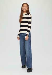 Zwart-wit gestreepte geribbelde trui met lange mouwen, gecombineerd met losse blauwe jeans en zwarte laarzen met stevige zool.