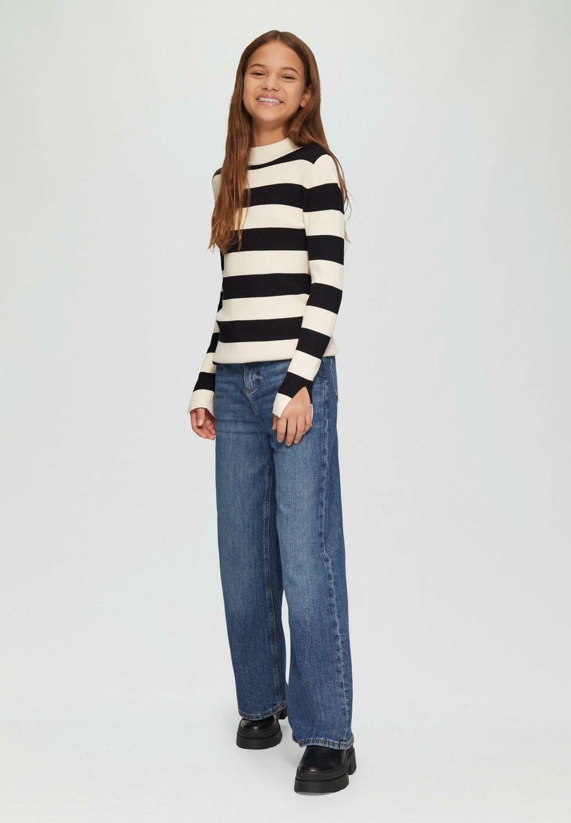 Zwart-wit gestreepte geribbelde trui met lange mouwen, gecombineerd met losse blauwe jeans en zwarte laarzen met stevige zool.