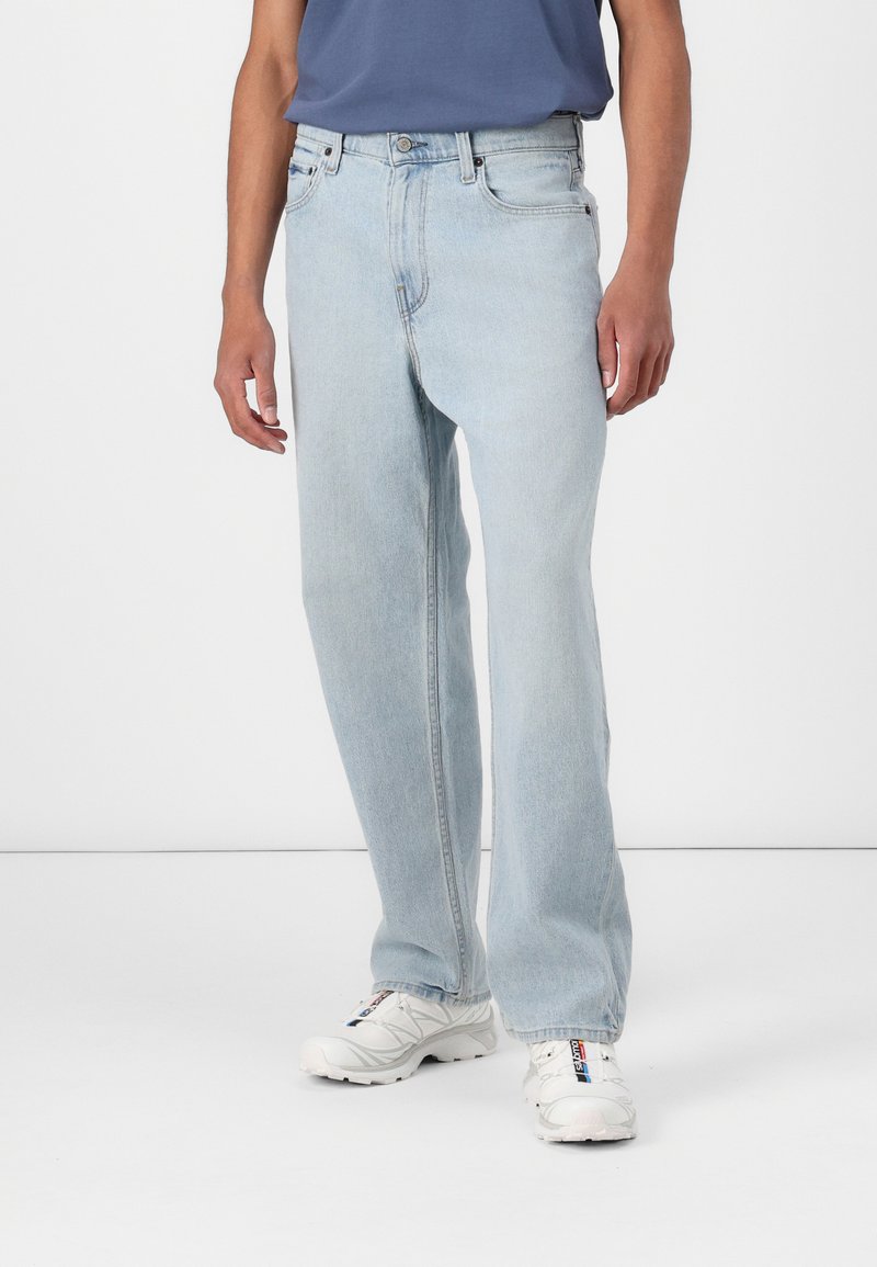 Lyseblå denimjeans med rett ben-design, enkel frontlomme og knapp- og glidelåsåpning. Brukt sammen med hvite joggesko.