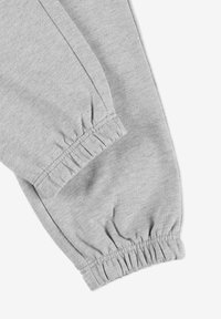 Szare bawełniane spodnie dresowe z elastycznymi mankietami przy kostkach, mają miękką, szczotkowaną teksturę oraz widoczne szwy wzdłuż krawędzi.