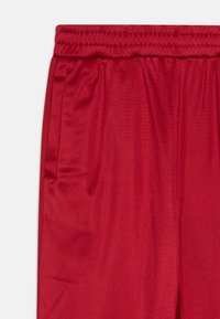 Sarkanas sporta bermudas ar elastīgu jostu, kurām ir divas sānu kabatas un gluda, viegla auduma tekstūra.