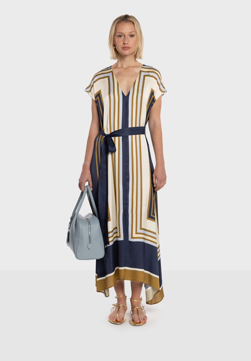 Abito lungo con scollo a V e maniche corte, caratterizzato da strisce verticali oro, blu navy e bianche. Abbinato a una borsa azzurro chiaro e sandali dorati.