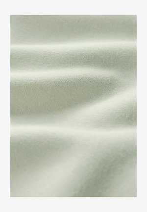 Tela suave de color verde claro con textura de punto fino y pliegues suaves que crean sombras y reflejos sutiles.