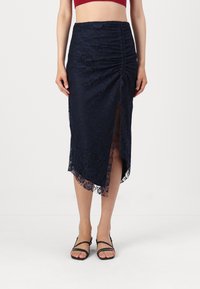 Ναυτική μεσάτη φούστα από δαντέλα με ρυάκια, πλαϊνό σκίσιμο και κροσσες στο τελείωμα. Διαθέτει διάφανη υφή δαντέλας και συνδυάζεται με μαύρες σανδάλες με λουράκια.