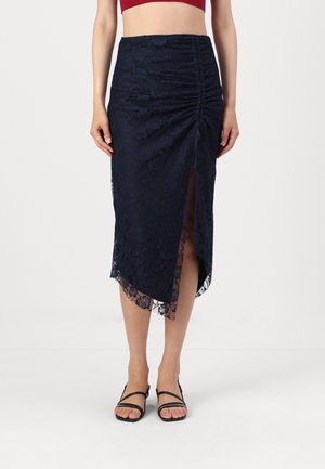 Navy lace midi skirt with ruched detailing, side slit, and scalloped hem. Features sheer lace texture and is paired with black strappy sandals.