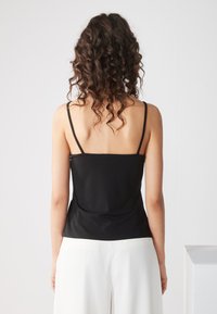 Camisetta nera aderente con spalline sottili e una texture liscia, che arriva fino alla vita, abbinata a pantaloni bianchi a gamba larga.