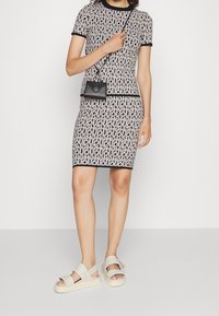 Schwarz-weißer, gemusterter, taillierter Kleid mit kurzen Ärmeln, schwarzem Besatz und einer schwarzen Umhängetasche, kombiniert mit hellgrauen Plateausandalen.