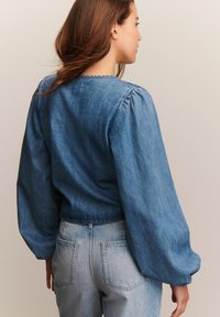 Denim majica s napuhanim rukavima, koja ima okrugli izrez. Nosena je s svijetloplavim trapericama, oboje prikazuje izblijedjeli izgled.