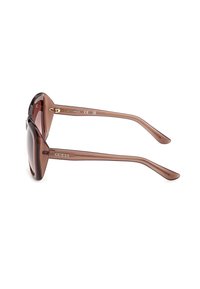Lunettes de soleil surdimensionnées translucides marron avec verres dégradés, branches fines et marquage "GUESS" sur les branches.