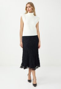 Cima senza maniche di colore bianco con collo alto abbinata a una gonna midi di pizzo nera. Tacchi a punta neri completano l'outfit. Il pizzo testurizzato mostra dettagli intricati.