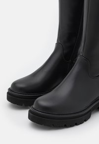 Botas de goma negras con una textura suave, punta redondeada y suela gruesa. Cuentan con un zip lateral para facilitar su uso. Detalle de costura reforzada.