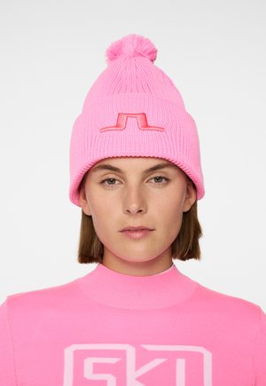 Bright pink knitted beanie with a pom-pom on top and a raised logo detail on the front. Ribbed texture throughout the fabric.