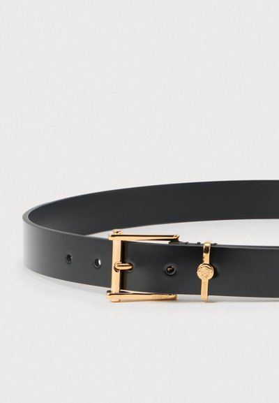 Fekete bőröv fényes kivitelben, aranyszínű fémcsattal és jellegzetes díszítésekkel, köztük egy logómedállal.