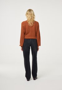 Roodbruine geribbelde trui met lange mouwen en een ontspannen pasvorm, gecombineerd met hooggesneden zwarte rechte broek.