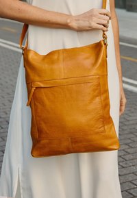 Borsa a tracolla in pelle marrone con una superficie liscia, forma rettangolare e tasca esterna. È dotata di una tracolla e di un design senza cuciture.