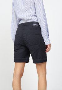 Černé džínové kraťasy s ohrnutými lemy, dvěma zadními kapsami a značkovou záplatou na pase, kombinované s pruhovaným tričkem s dlouhým rukávem.