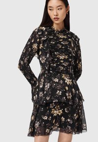 Vestido floral en negro con flores amarillas y blancas, con volantes en capas, corpiño plisado y mangas largas. Tela transparente con textura ligera.