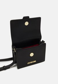 Borsa a tracolla in pelle nera con superficie testurizzata, hardware dorato, chiusura a scatto e fodera interna rossa. Presenta il logo "LOVE MOSCHINO".