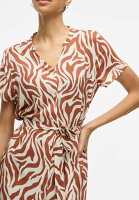 Kortärmad klänning i krämfärg med ett brunrandigt zebramönster, med V-ringning, knappar och detalj med knytning i midjan. Slät tygtextur.