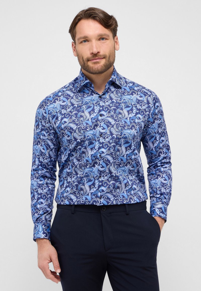Blauwe overhemd met een patroon van in elkaar overloppende paisley ontwerpen in verschillende tinten, lange mouwen en een button-down kraag. Gecombineerd met donkere broeken.