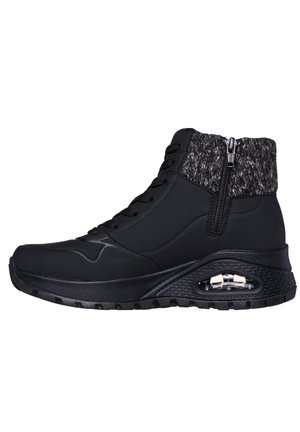 Bottes de sport noires avec une tige tricotée grise texturée, un devant à lacets, une fermeture éclair et un coussin d'air visible au niveau du talon.