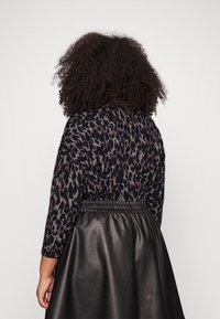 Pull imprimé léopard noir et gris à coupe décontractée, associé à une jupe noire haute taille en similicuir avec une ceinture élastique.