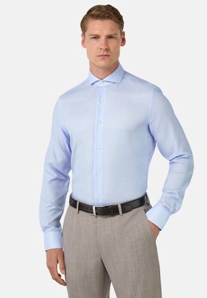 Hellblaues Hemd aus strukturiertem Stoff mit klassischem Kragen und langen Ärmeln, kombiniert mit hellgrauen Hosen und einem schwarzen Gürtel.