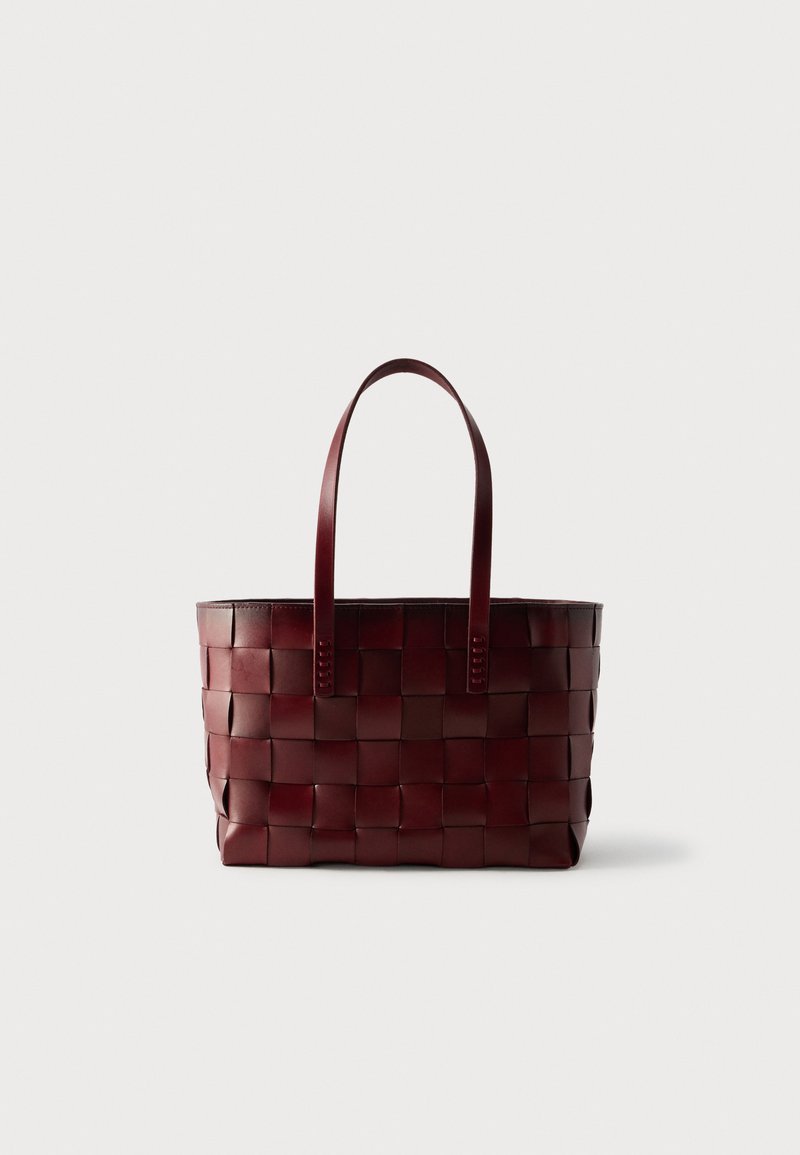 Πλεκτή τσάντα ώμου από σκούρο καφέ δέρμα με δύο λουράκια, τοποθετημένη σε απλό φωτεινό φόντο.