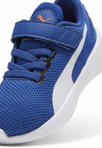 Zapatilla deportiva azul con parte superior de malla, acentos blancos y una correa de Velcro. Cuenta con tela texturizada y una suela acolchada y ligera.