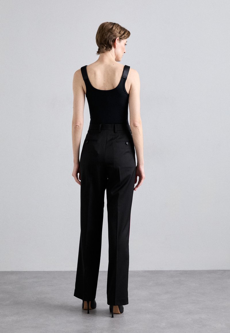 Body nero con spalline larghe, abbinato a pantaloni neri a vita alta. I pantaloni hanno una vestibilità sartoriale, tasche posteriori visibili e linee eleganti.