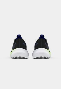 Zapatos deportivos negros con una textura suave, acentos verdes en la suela y una lengüeta azul. Diseño ligero con un talón acolchado.