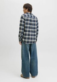 Rutede skjorte i blå og hvid, knaplukket, parret med oversized denimjeans. Jeansene har en bred benstil og en lys vask.