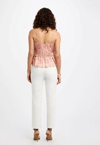 Top peplum con motivo floreale in rosa chiaro, con spalline sottili e vita arricciata, abbinato a pantaloni aderenti bianchi e tacchi beige.