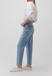 Vaqueros de tiro alto en azul claro con un ajuste relajado, perneras rectas y un ligero desgaste. Combinados con una camisa blanca de mangas abullonadas y zapatillas crema.