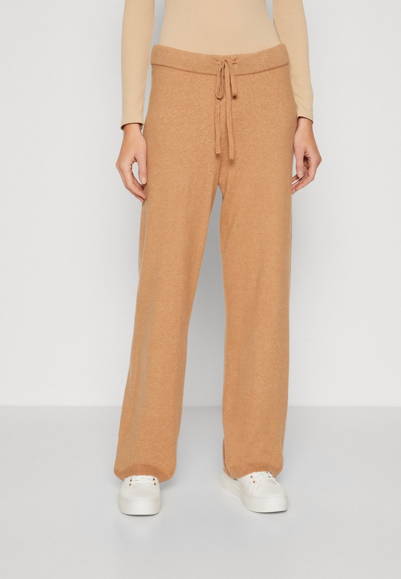 Lysebrune brede sweatpants med snor i taljen og ribbede manchetter, lavet af et blødt, struktureret stof. Sammen med hvide sneakers.
