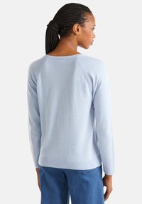 Pull léger bleu clair avec un col rond, des poignets et un ourlet côtelés. Il présente un design à manches raglan et une texture douce.