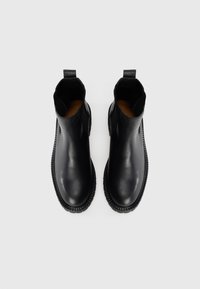 Botas de cuero negro hasta el tobillo con un acabado liso, paneles laterales elásticos y suelas de goma texturizadas. Presentan tiradores para facilitar su puesta.