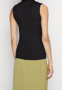 Top nero a coste senza maniche con collo alto, caratterizzato da una silhouette aderente. Abbinato a una gonna verde chiaro, con cuciture visibili all'orlo.