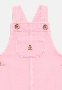 Rosa toddler jumpsuit med frontlomme, liten brodert brun kosedyr-design, og to brune knapper på skulderstroppene.